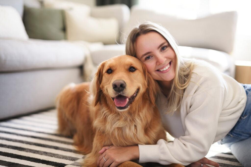 Frau sitzt mit einem Golden Retriever im Wohnzimmer